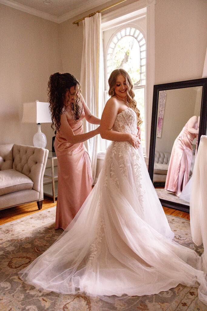 Bride getting zipped up by maid of honor during getting ready time for full wedding photography coverage