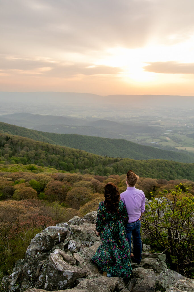 Golden sunset lights up the sky behind a couple embracing on a rocky overlook in Shenandoah National Park.