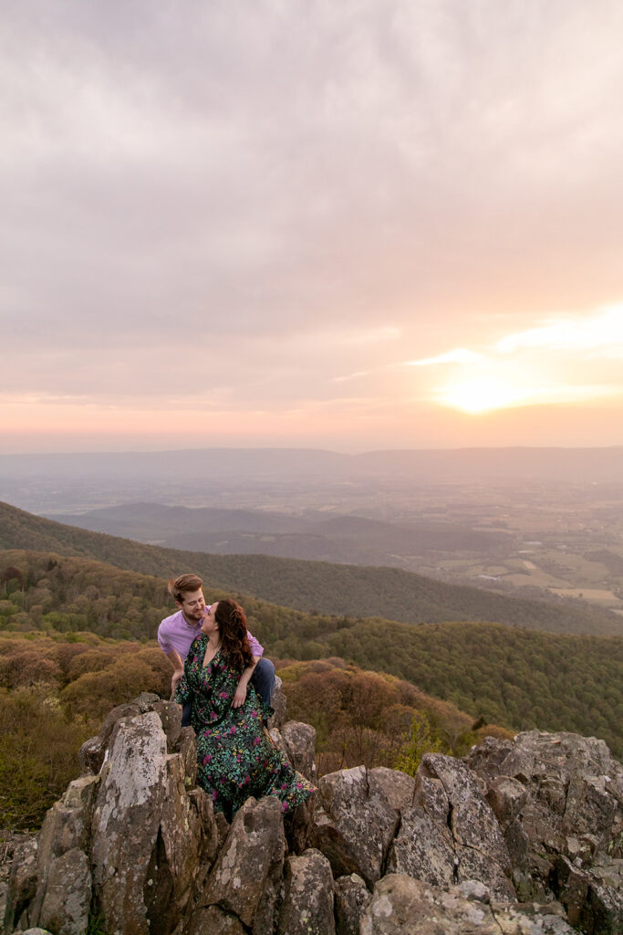 Engaged couple sits together, admiring the vast mountain views from Little Stony Man summit at sunset.