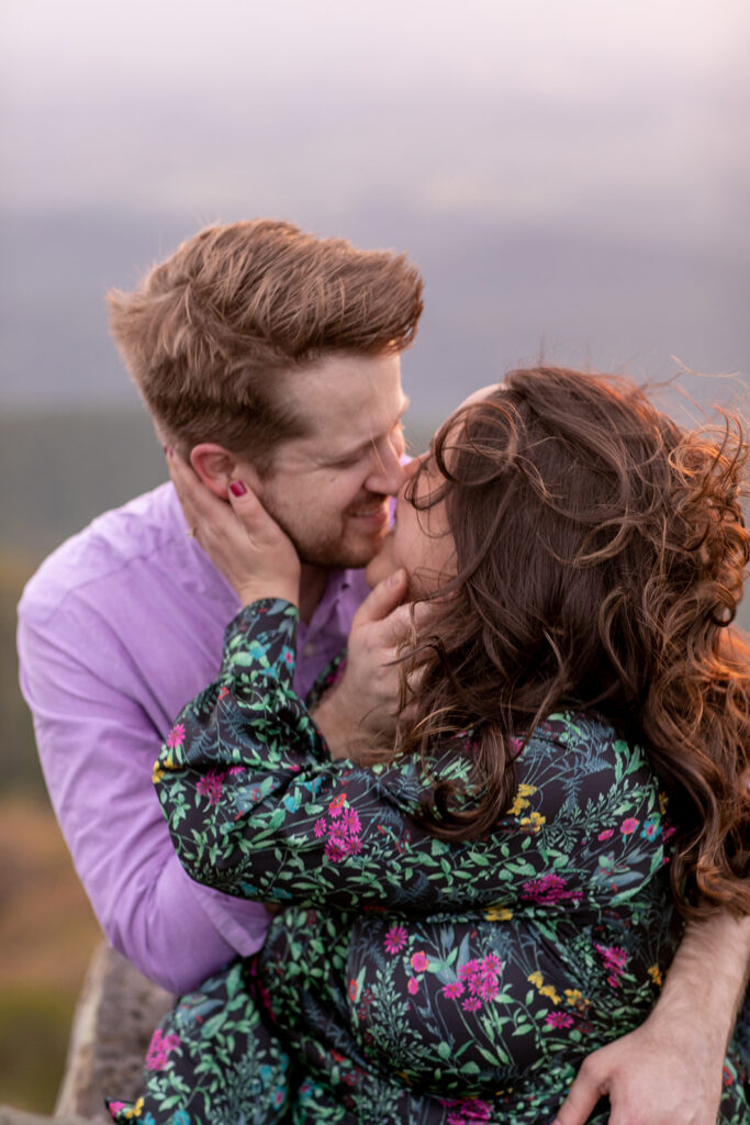 Engaged couple shares a romantic kiss at Little Stony Man summit, framed by the breathtaking Shenandoah landscape