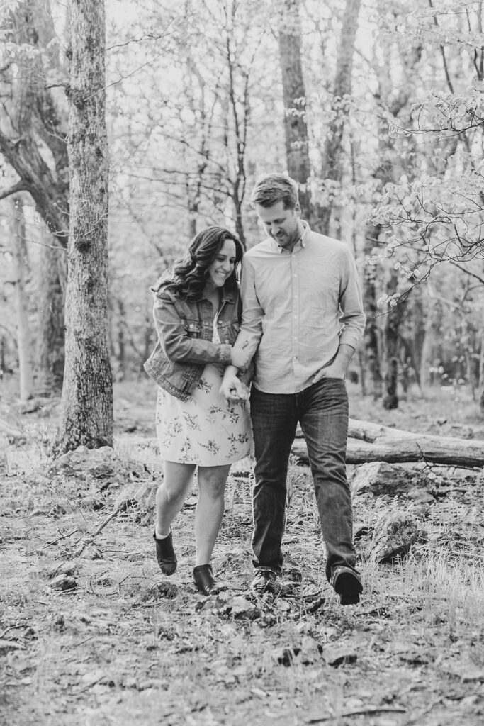 Engaged couple walks hand in hand through lush spring greenery at the base of Little Stony Man trail in Shenandoah National Park.