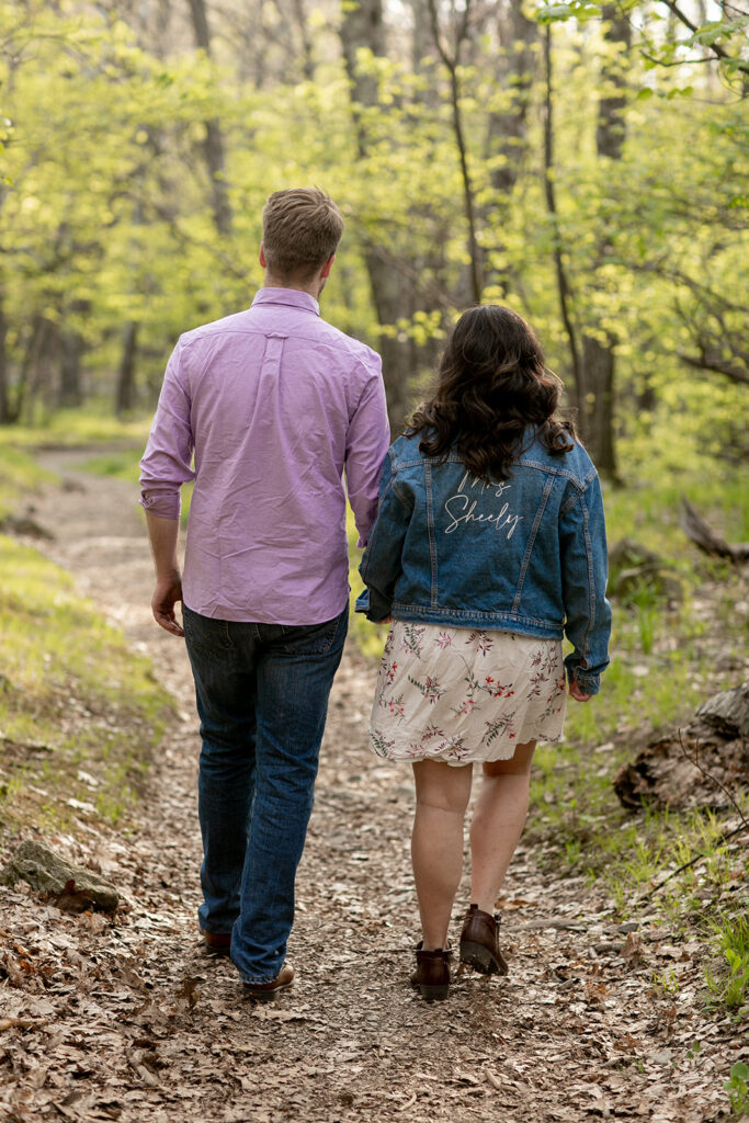 Playful engaged couple walks through Shenandoah’s vibrant May landscape, soaking in the adventure.