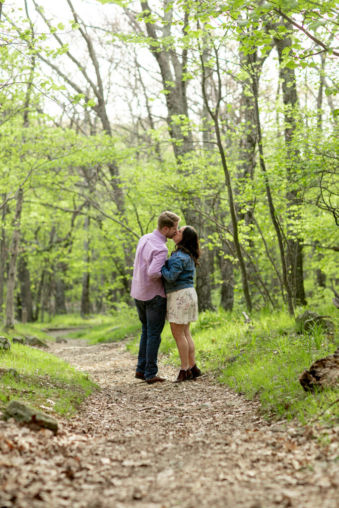 Couple pauses for a kiss as they walk along a scenic forest path in Shenandoah’s spring landscape.