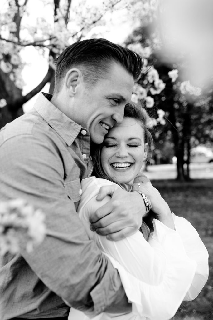 Playful and candid engagement session among cherry blossoms in a quiet DC park