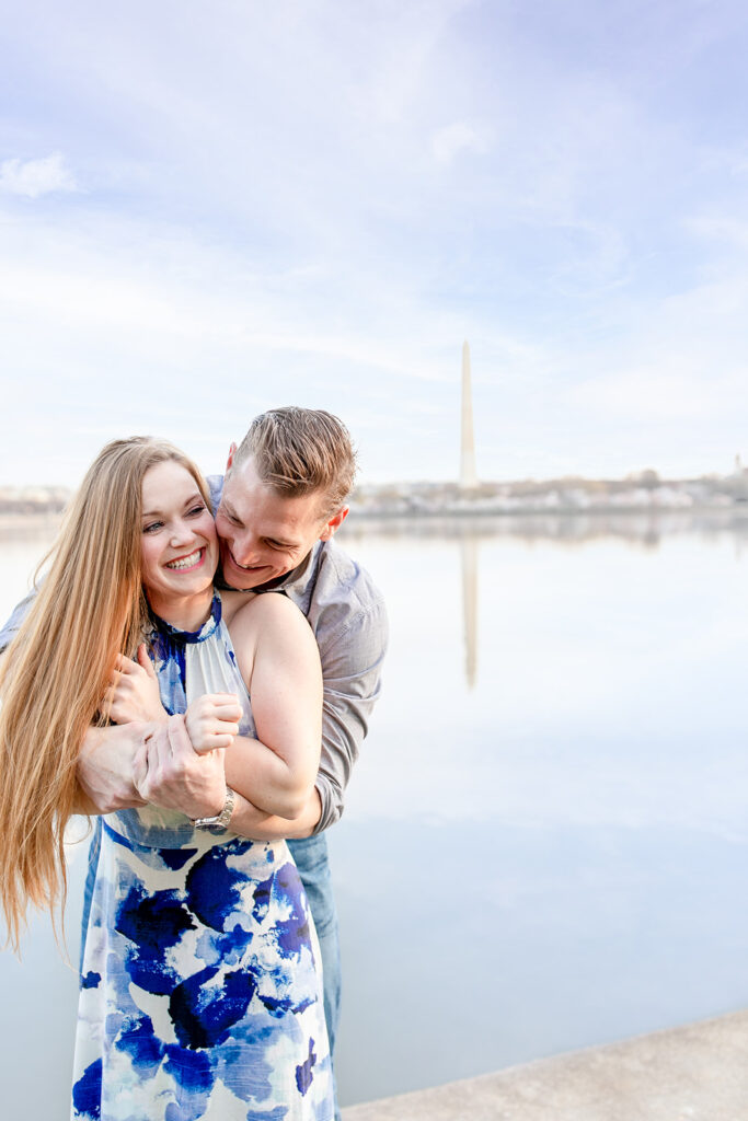 Bride and groom playfully embracing during a sunrise engagement session during the DC Cherry Blossom festival with the Washington Monument framed in the background across from the tidal basin