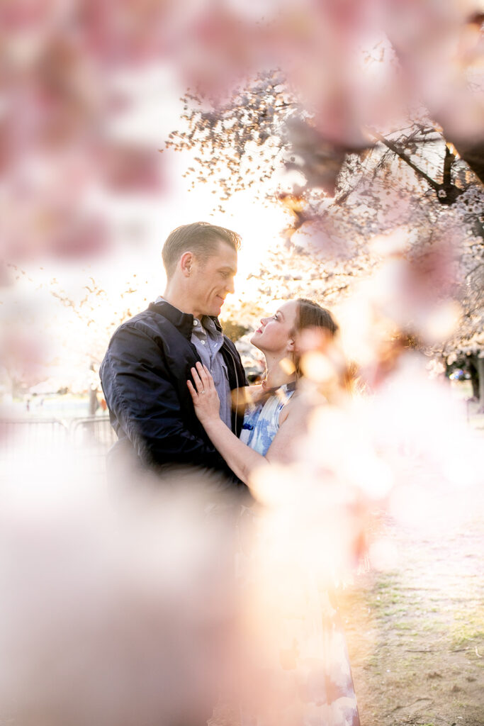 Engaged couple posing under blooming cherry blossom trees at the Tidal Basin in Washington, DC