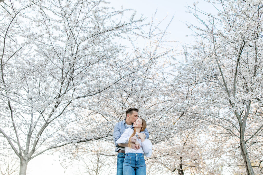 Bride and groom embrace in front of cherry blossoms during engagement session at the DC Cherry Blossom festival in the spring