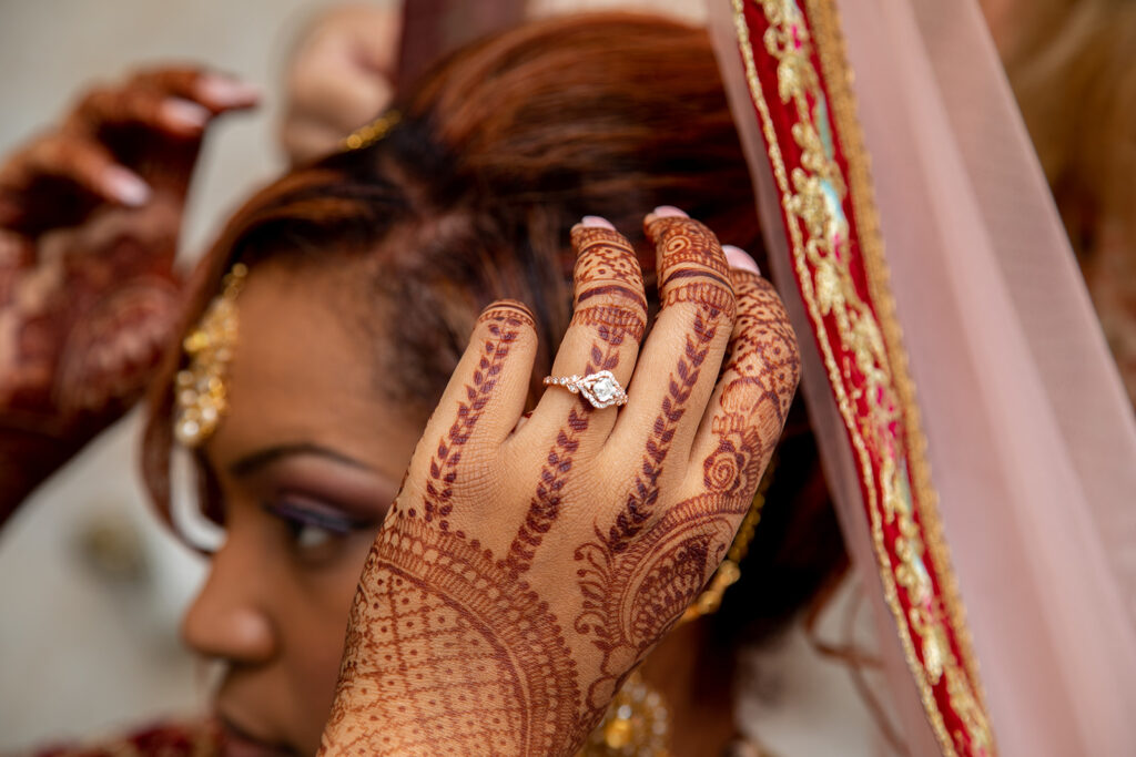 Emotional moment of bride’s mother-in-law helping her put on traditional wedding headdress, with close-up of hands and engagement ring during prep in Northern Virginia