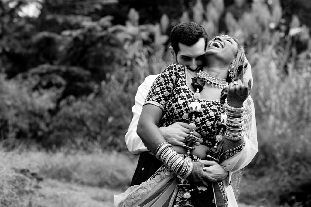 Candid shot of bride and groom laughing together during golden hour portraits in the landscaped garden