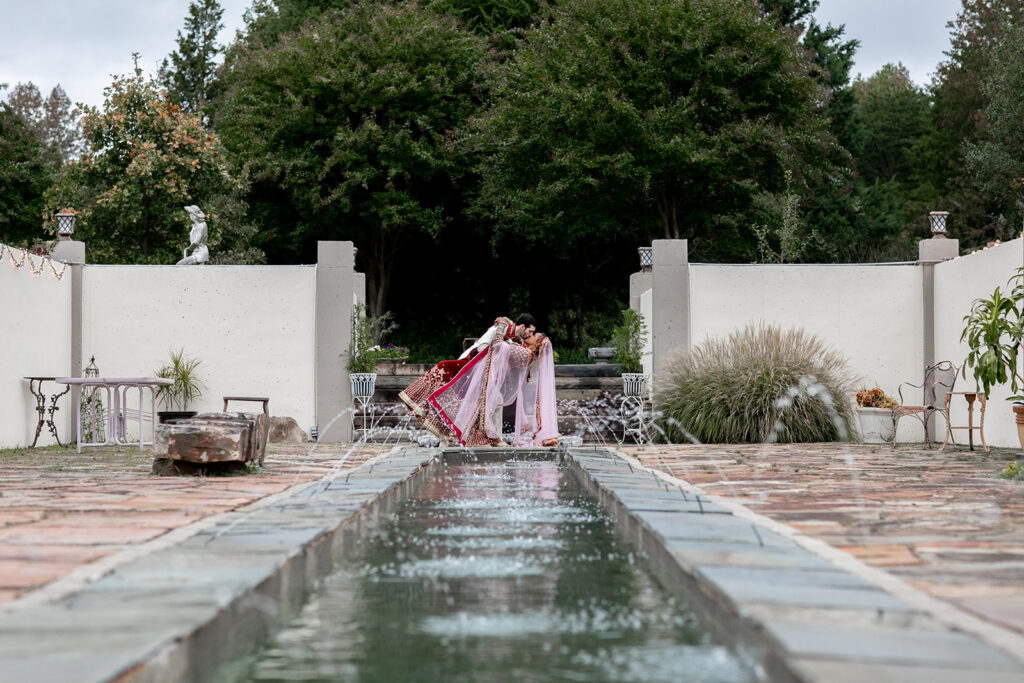 Bride and groom portrait with groom dipping bride for a kiss in front of fountain in a garden wedding in Northern Virginia