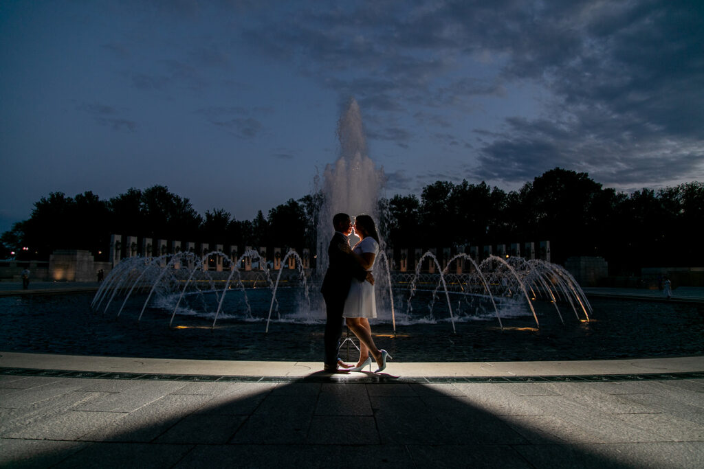 Engaged couple dancing in front of illuminated World War II Memorial fountain in Washington, DC at dusk