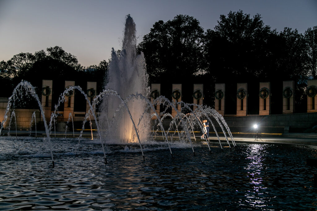 DC couple embracing in front of the glowing fountains at the World War II Memorial during their iconic monument engagement session