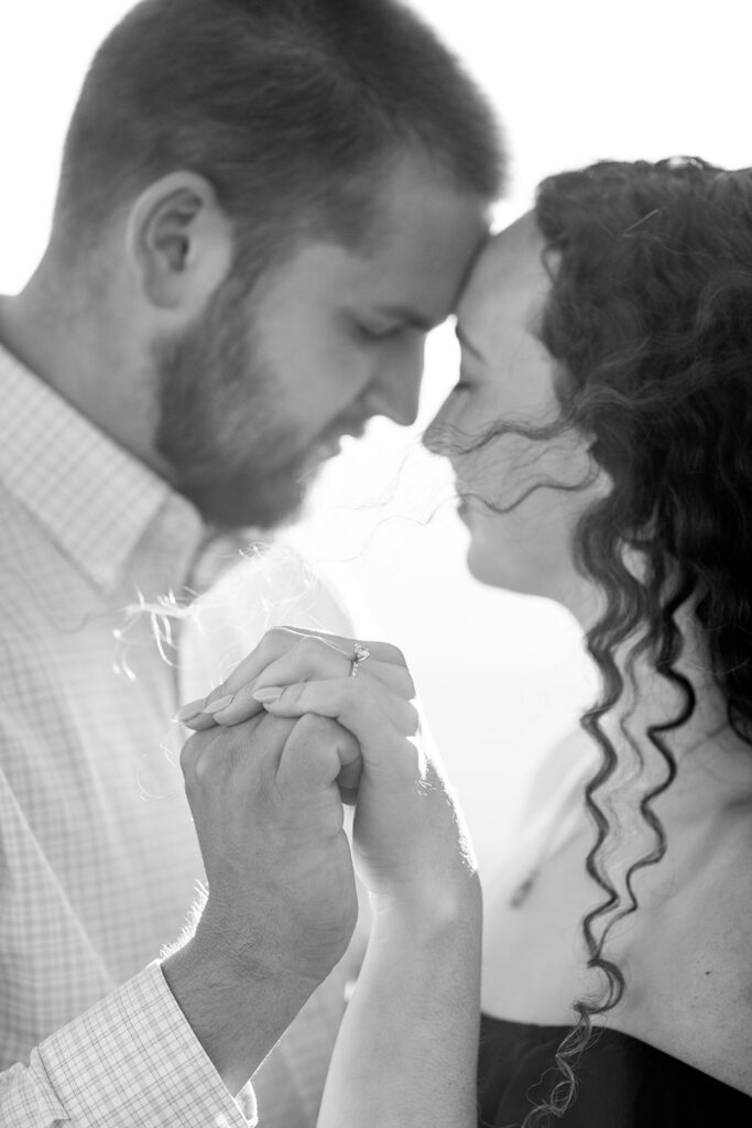 Black and white close-up of engaged couple holding hands and touching foreheads during emotional moment