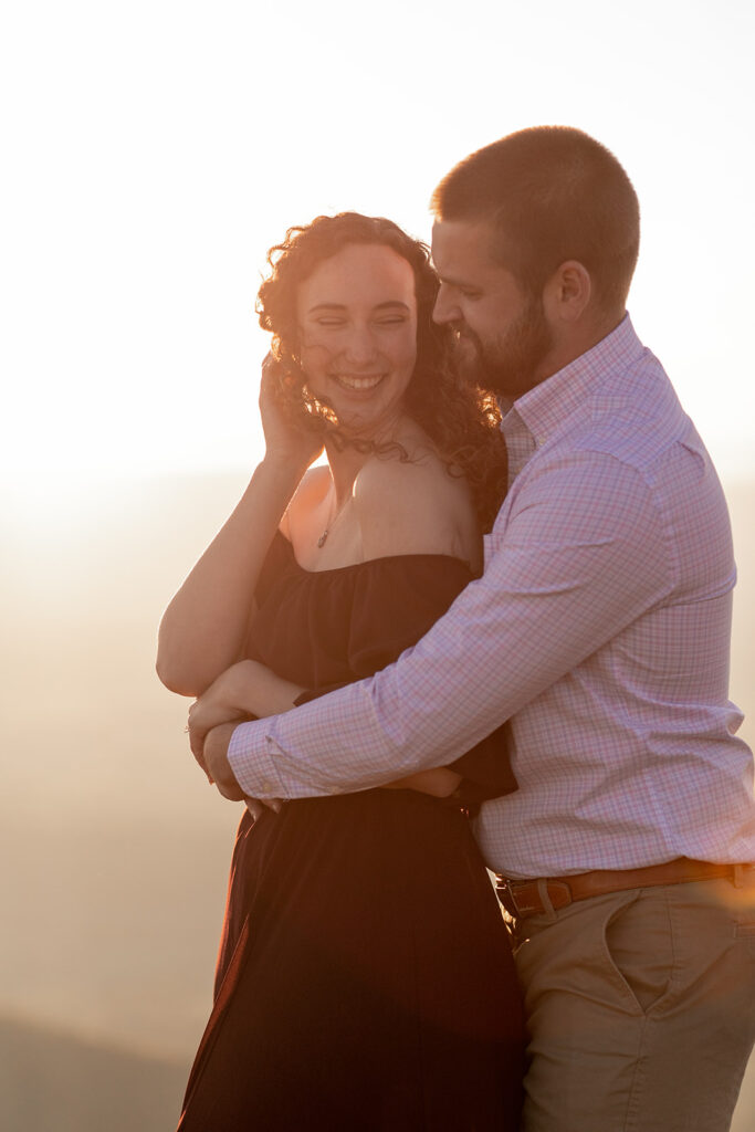 Bride-to-be laughing while being embraced during sunset engagement session in Shenandoah National Park