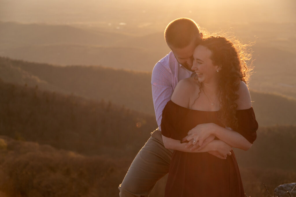 Golden hour laughter between engaged couple wrapped in a hug during mountaintop Shenandoah engagement session