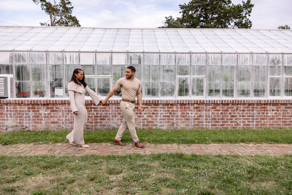 Engaged couple holding hands and walking near a greenhouse during a DC area engagement session