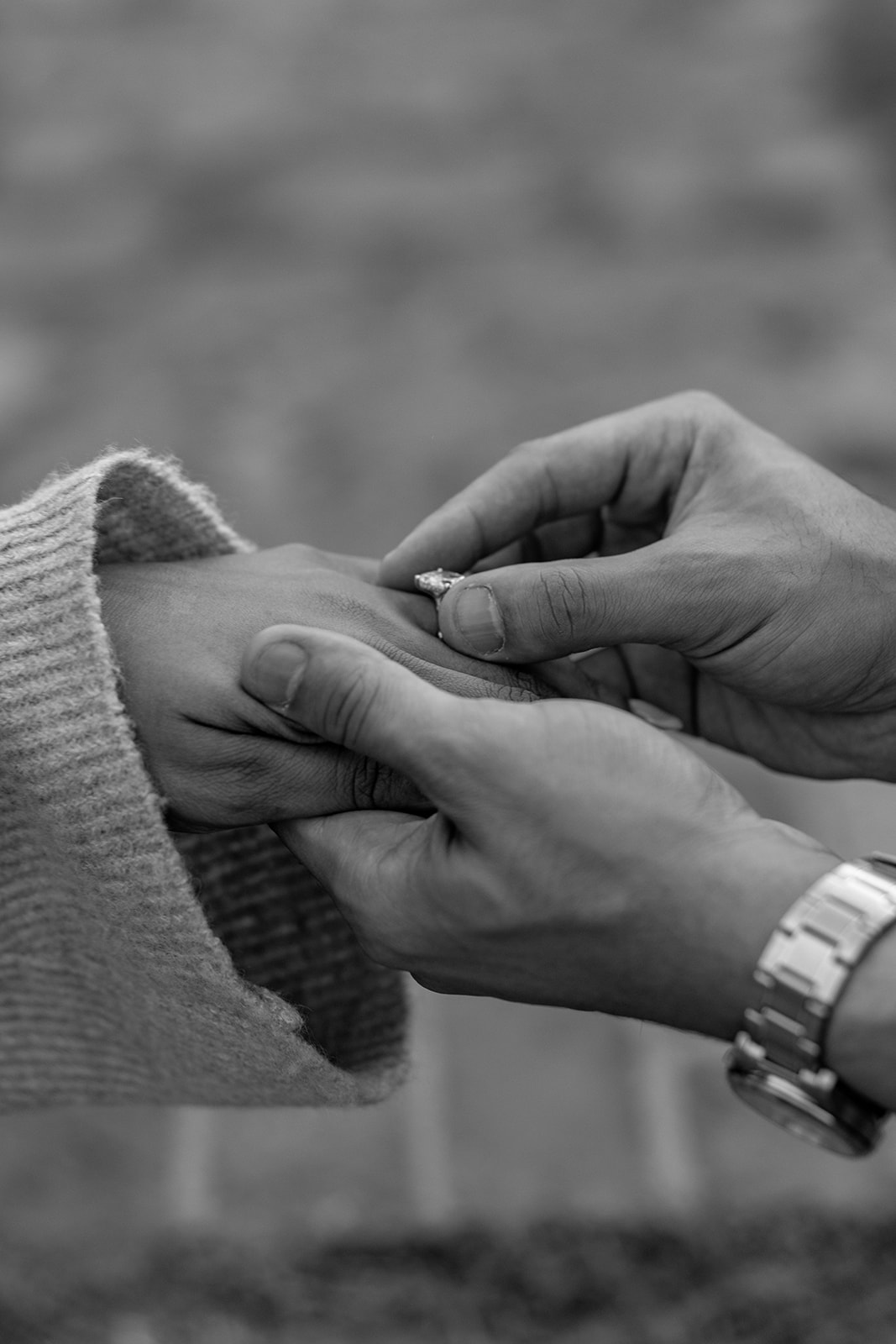 Man putting an engagement ring on fiance's finger during surprise proposal