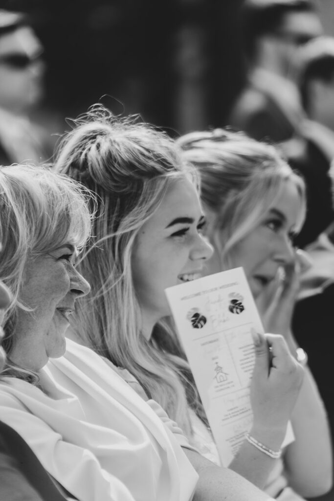 Wedding guests smiling and reacting emotionally during the ceremony, black-and-white candid.
