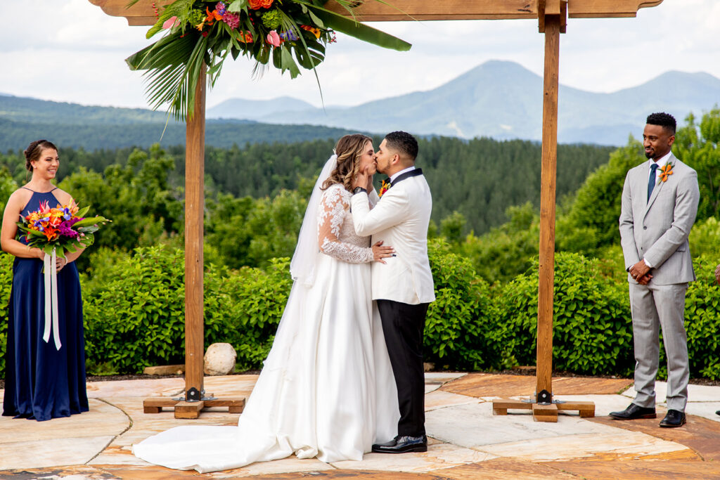 Bride and groom sharing their first kiss under the wooden ceremony arch.