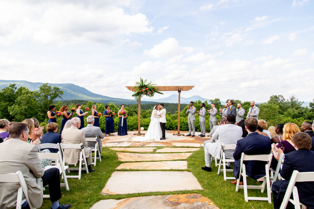 Wide ceremony view of the couple at the altar surrounded by wedding party and mountains.