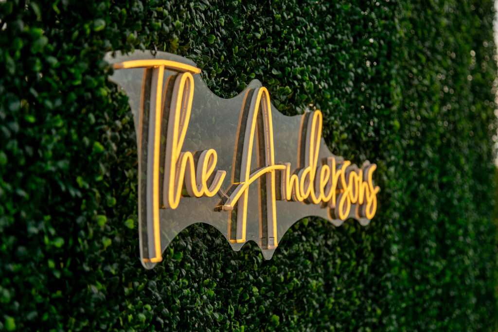 Neon “The Andersons” sign displayed on a green boxwood wall at the wedding reception.