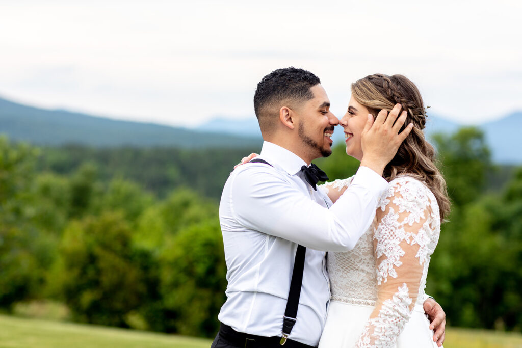 Groom holding the bride’s face during an intimate moment with green mountain scenery behind them.
