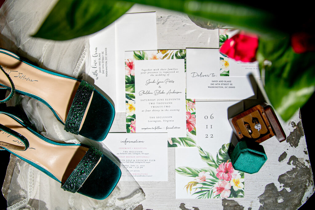 Emerald bridal shoes, tropical invitation suite, and velvet ring box styled together on a lace backdrop.