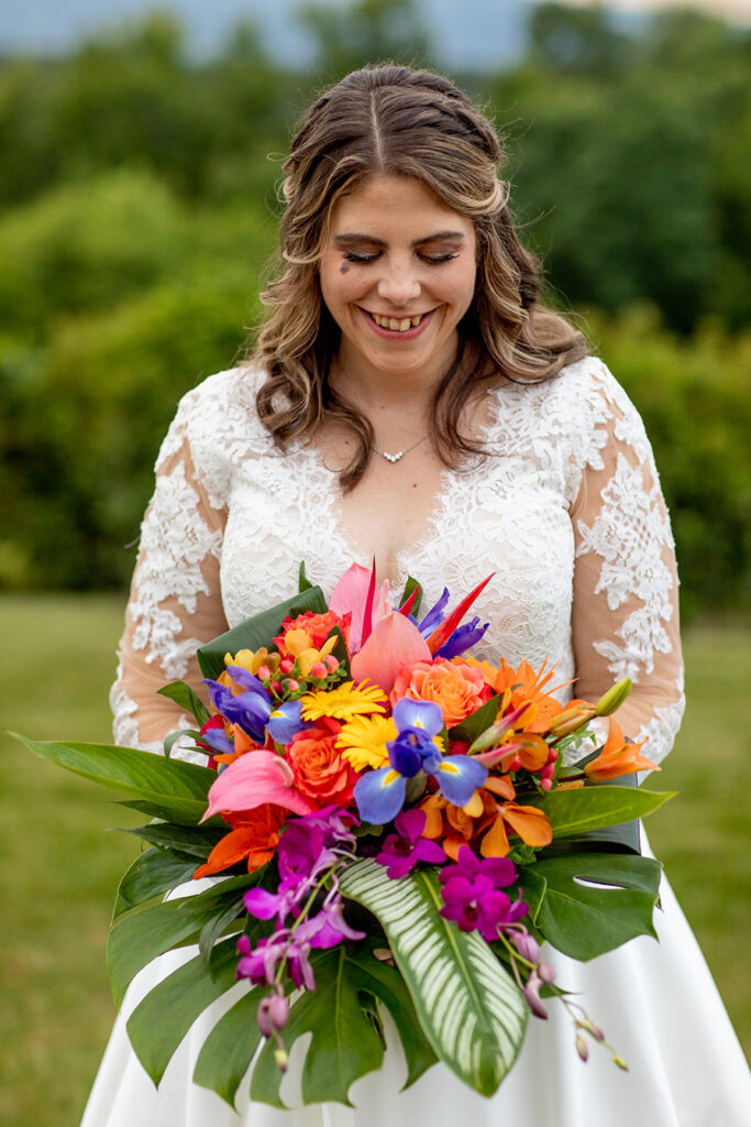 Bride holding a colorful tropical bouquet while smiling and looking down.