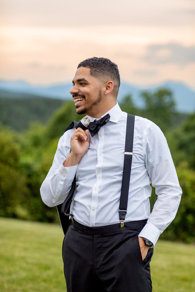 Groom laughing and holding his suit jacket over his shoulder while standing in front of mountain views.
