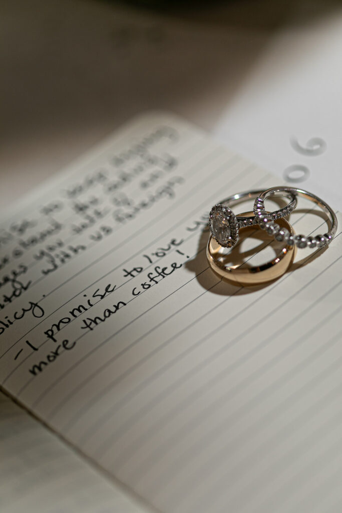 Wedding rings placed on handwritten vows that include a note saying “I promise to love you more than coffee.”