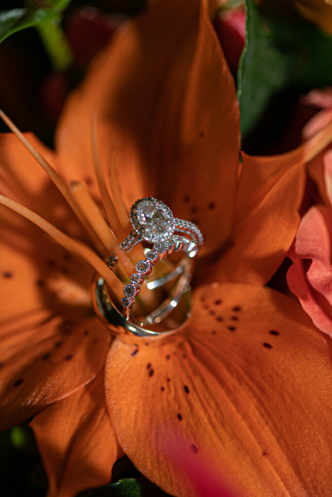 Engagement ring and wedding bands resting on an orange lily flower.