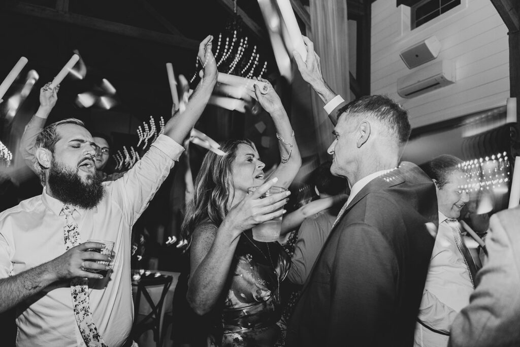 Guests cheering and dancing with raised arms on the dance floor, black-and-white image.