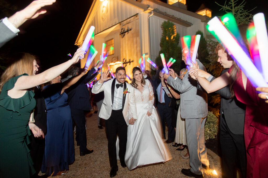 Bride and groom walking through a glow stick exit as guests cheer outside The Seclusion at night.