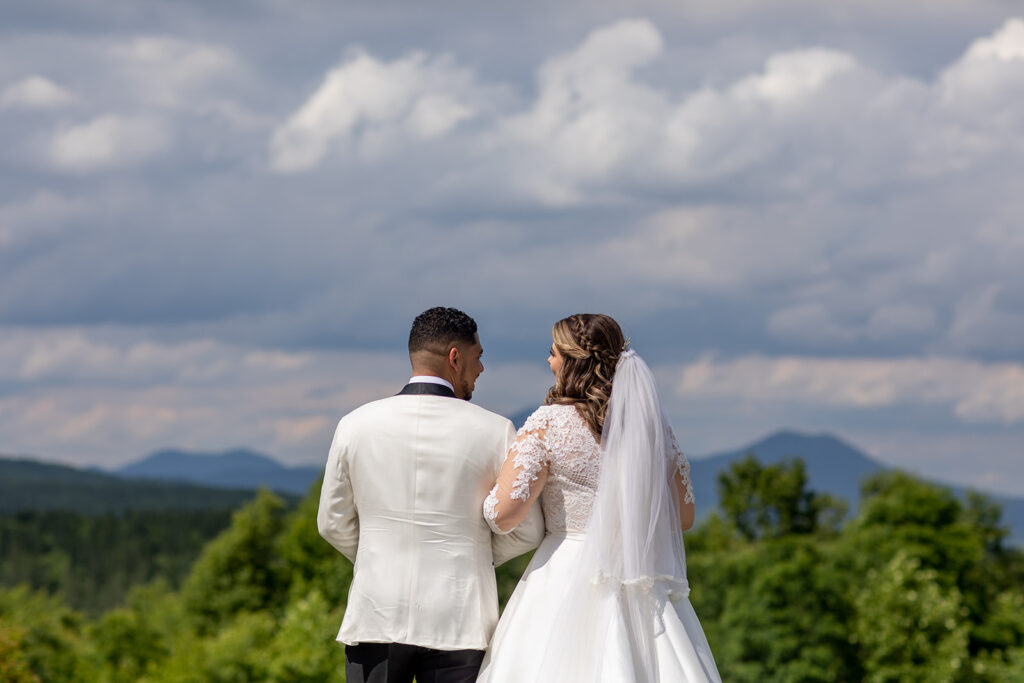 Groom and bride standing together facing the mountains under dramatic cloudy skies.