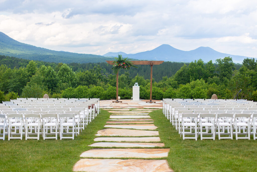 Outdoor ceremony setup at The Seclusion in Lexington, VA, with white chairs, a wooden arch decorated with tropical greenery, and Blue Ridge Mountain views in the background.