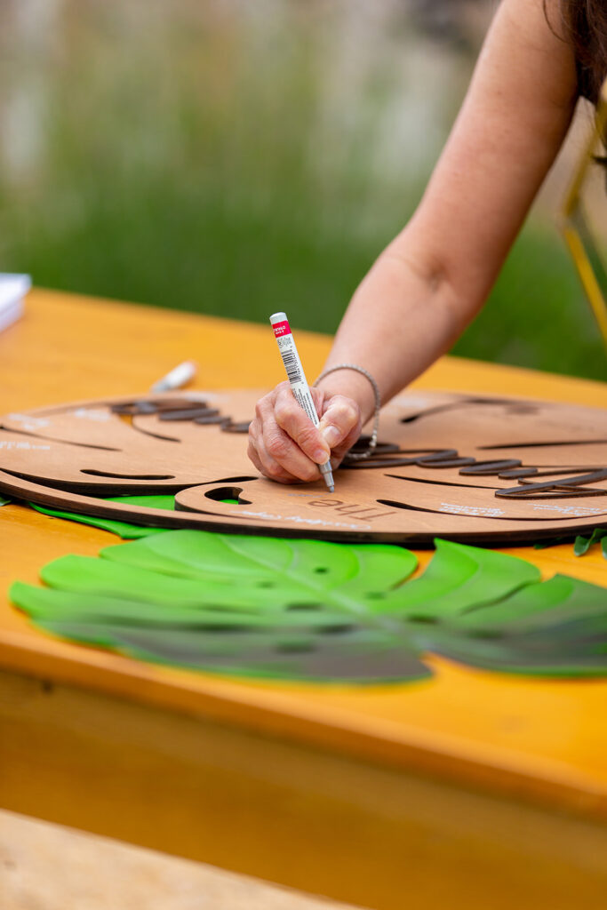 Guest signing a wooden guestbook surrounded by tropical leaf decorations.