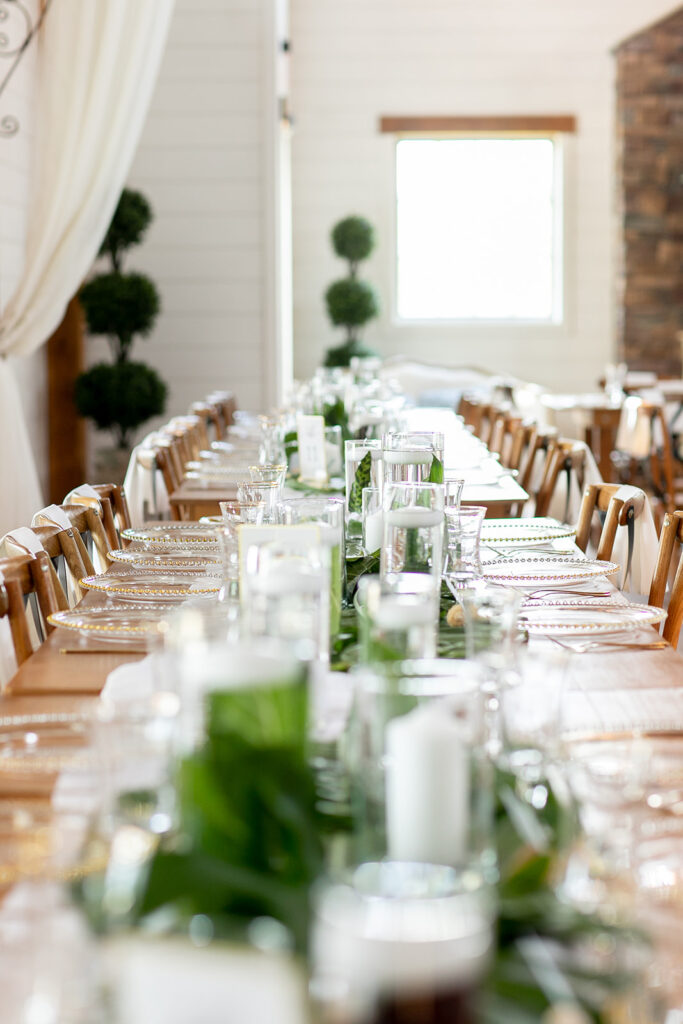 Long reception table set with white linens, candles, and tropical greenery running down the center.