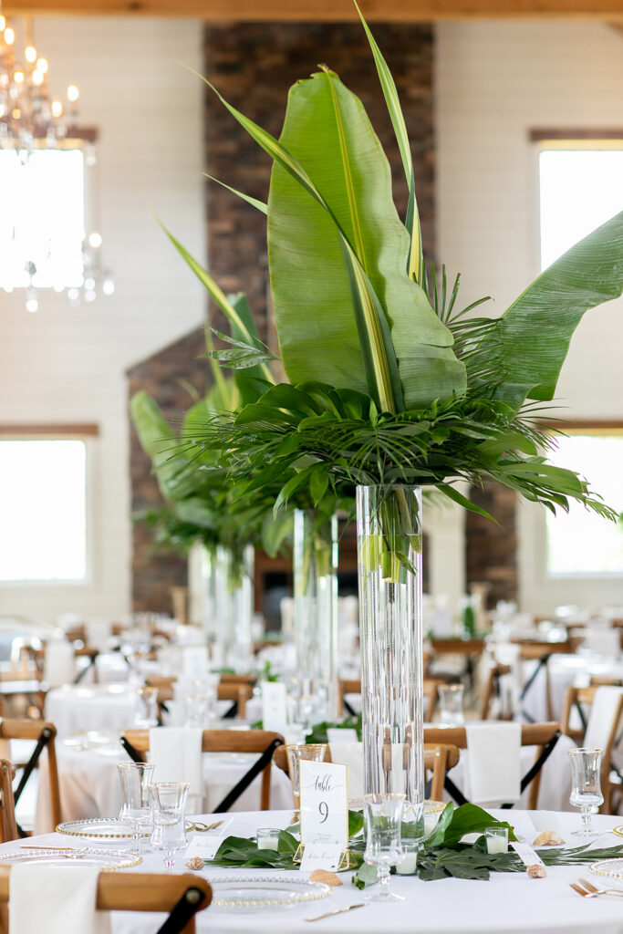 Tall glass centerpiece filled with tropical greenery inside The Seclusion’s reception hall.