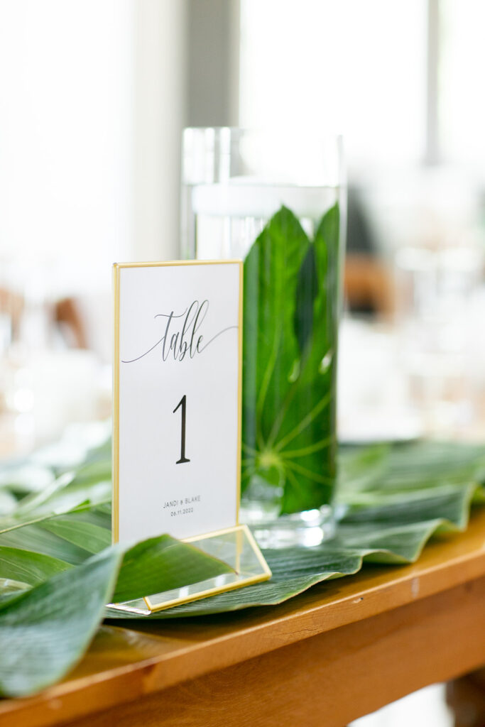 Table number display surrounded by layered tropical leaves and floating candles.