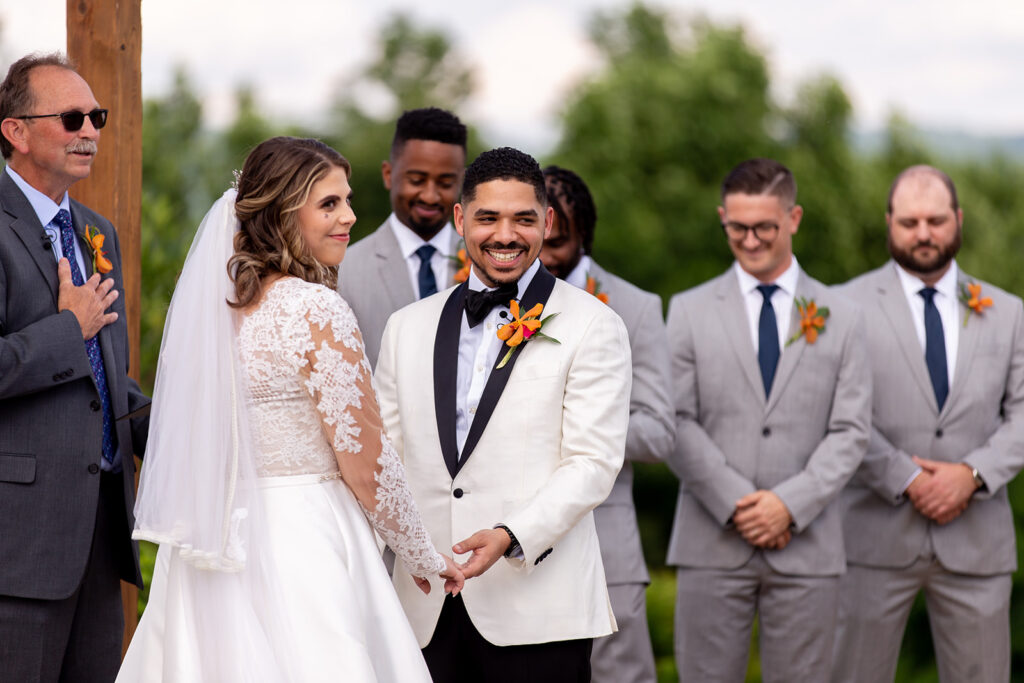 Bride and groom smiling at each other at the altar while the wedding party looks on.
