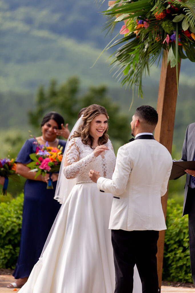 Bride laughing with the groom during their ceremony with vibrant greenery behind them.