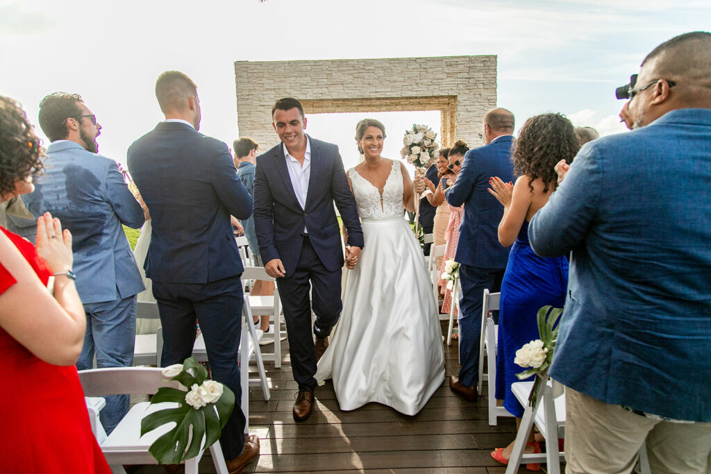 Bride and groom walking up the aisle celebrating, holding hands and smiling.