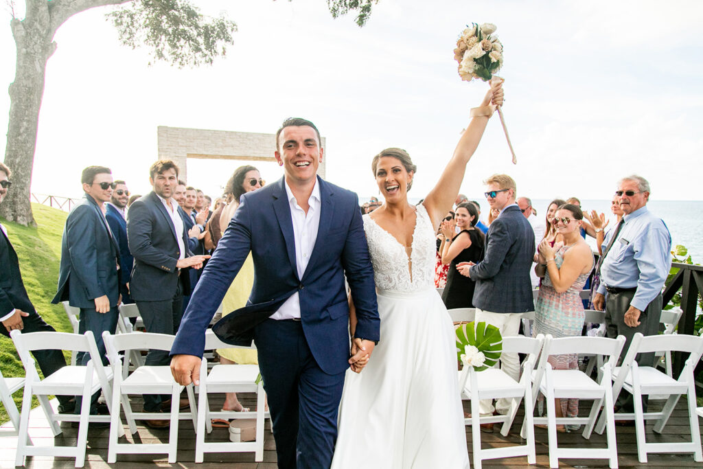 Bride lifting her bouquet triumphantly during the recessional as guests clap.