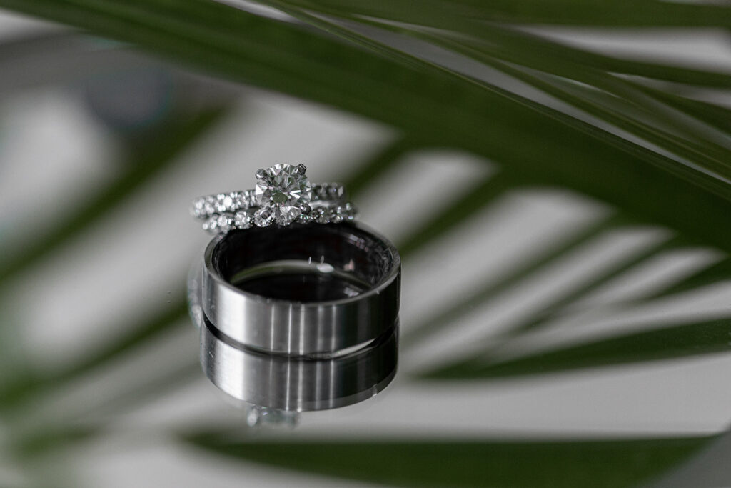 Close-up of the wedding rings stacked together with palm leaves reflecting in the background.