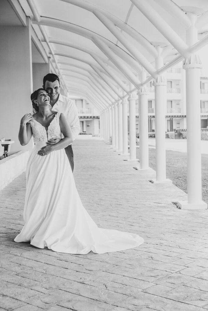 Bride and groom posing under the white arched walkway outside the resort.