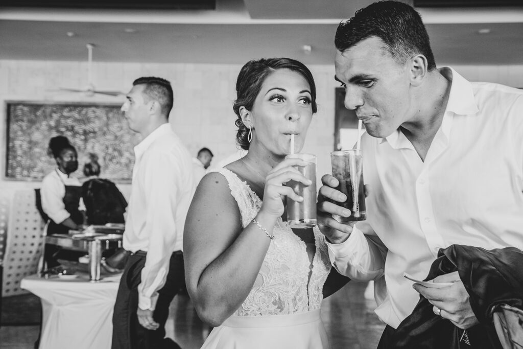 Bride and groom sipping cocktails together inside the reception hall.