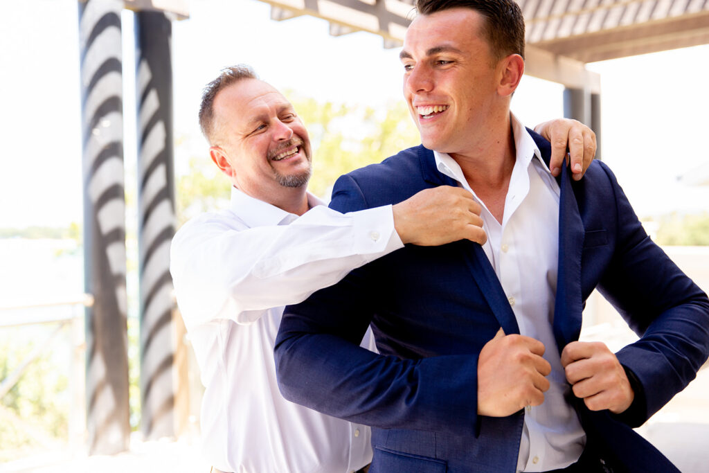 Groom’s father helping him adjust his suit jacket before the ceremony.