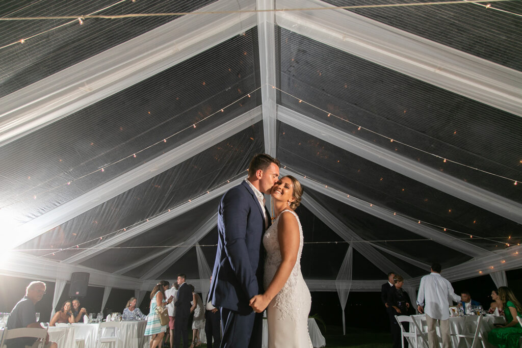 Bride and groom sharing their first dance under a clear tent with string lights.