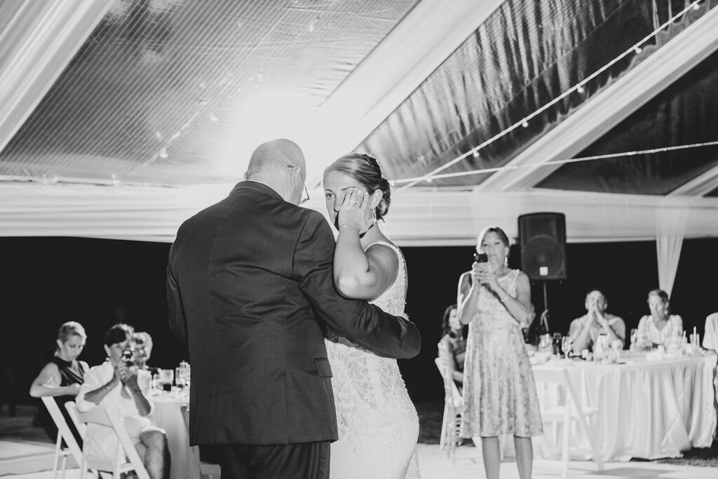 Father-daughter dance under the clear tent with guests watching.
