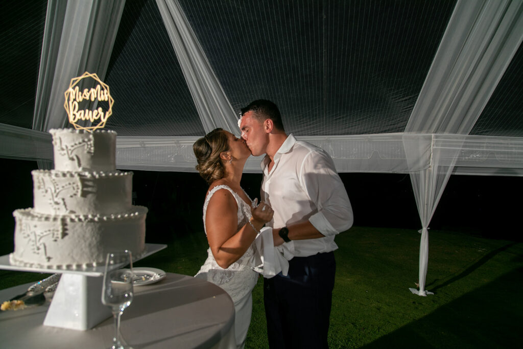 Wedding couple share a cake filled kiss after their cake cutting.
